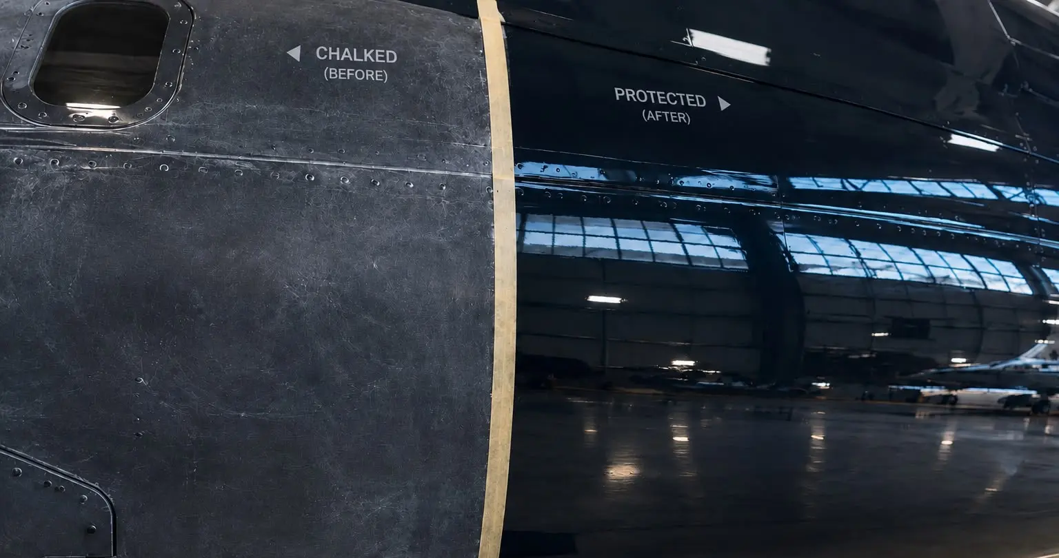 A business jet fuselage divided by masking tape: the chalked, matte section labelled before on the left, the coated section on the right returning the hangar roof as a clean reflection