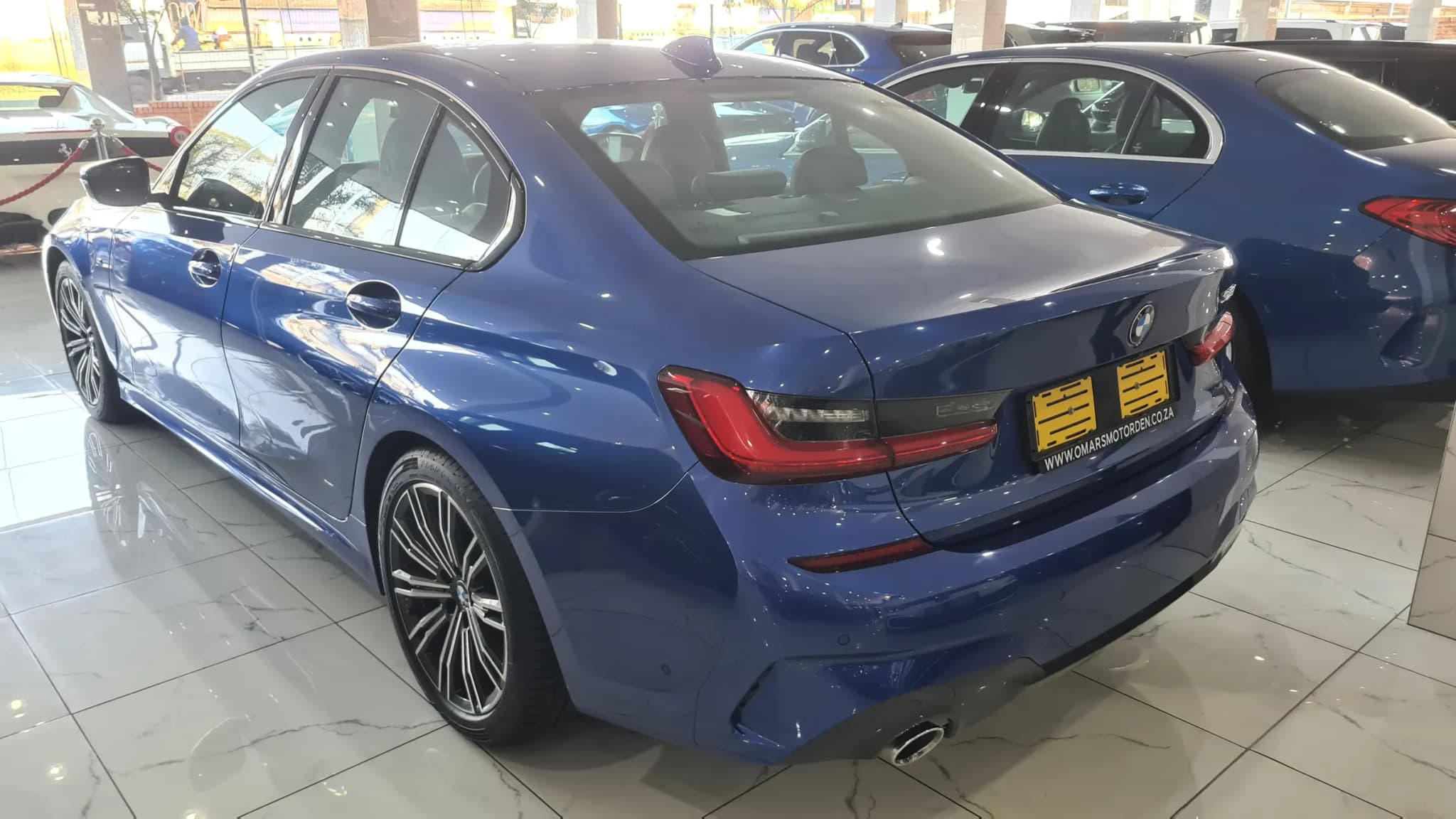 The same blue BMW 3 Series on the showroom floor after correction, the paint returning a clean reflection