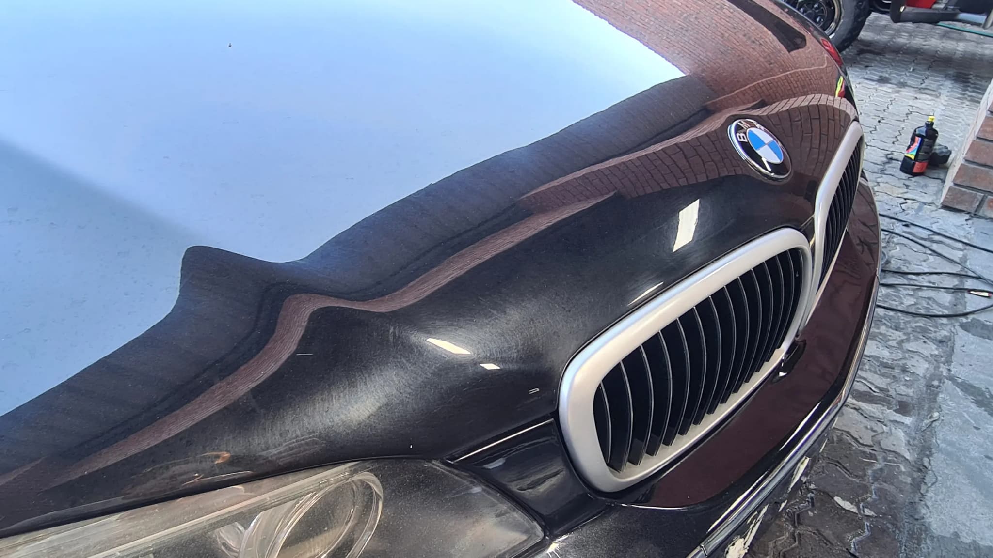 Raking sunlight across the uncorrected black bonnet of a BMW 7 Series, showing the haze left by years of automated washing