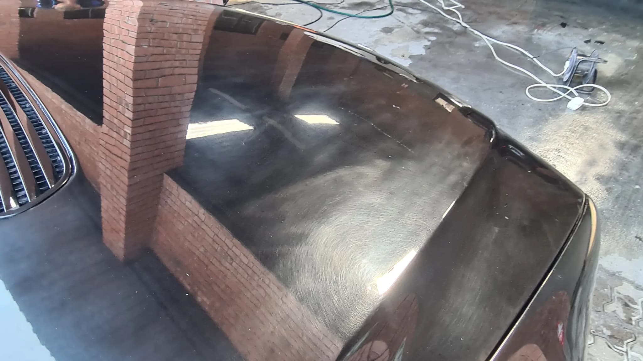 The bootlid of a black BMW 7 Series before correction, the brickwork behind it breaking up in the reflection
