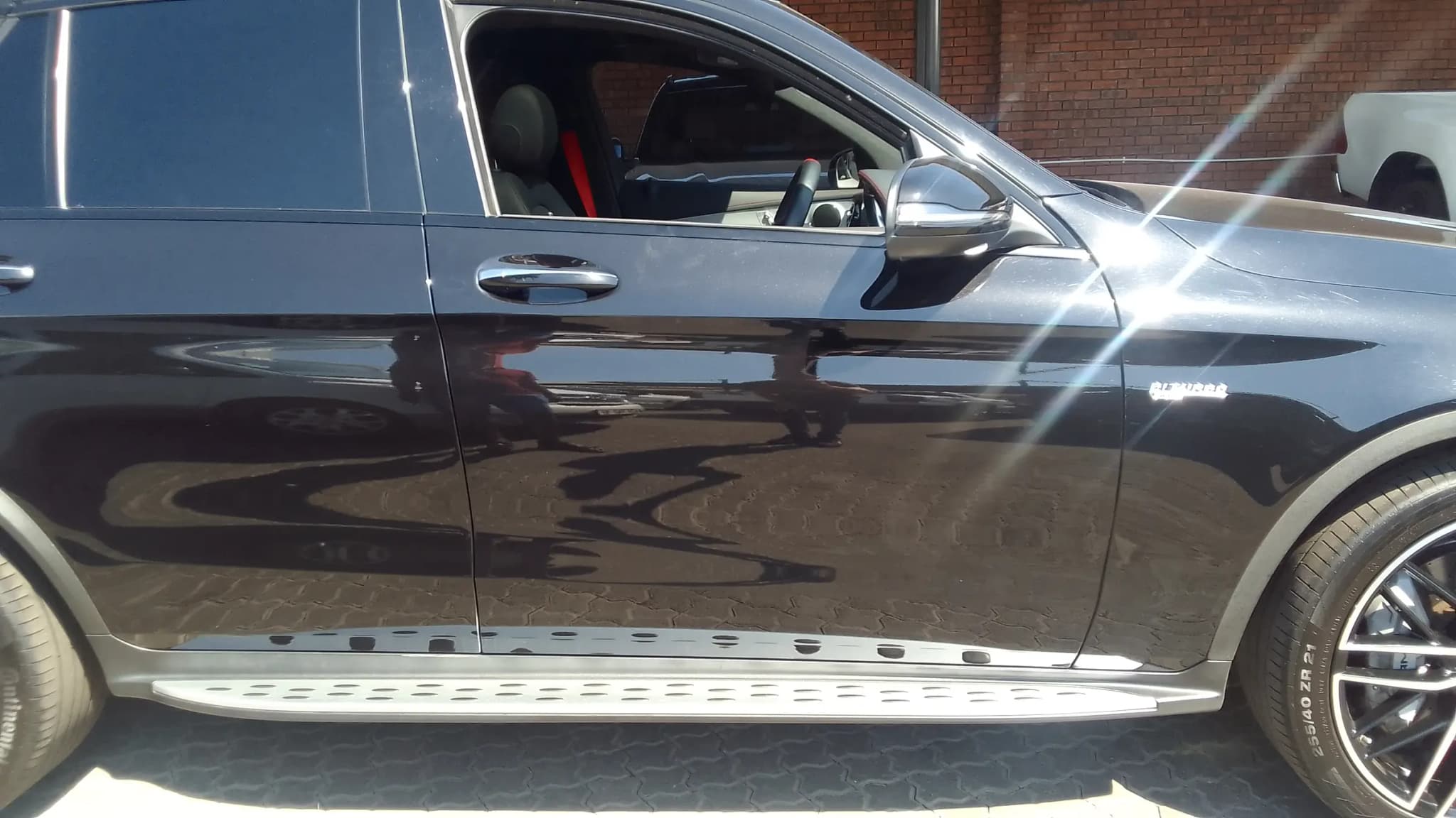 Raking sunlight across the uncorrected flank of a black Mercedes-AMG GLC 43, the marring in the clear coat scattering the light