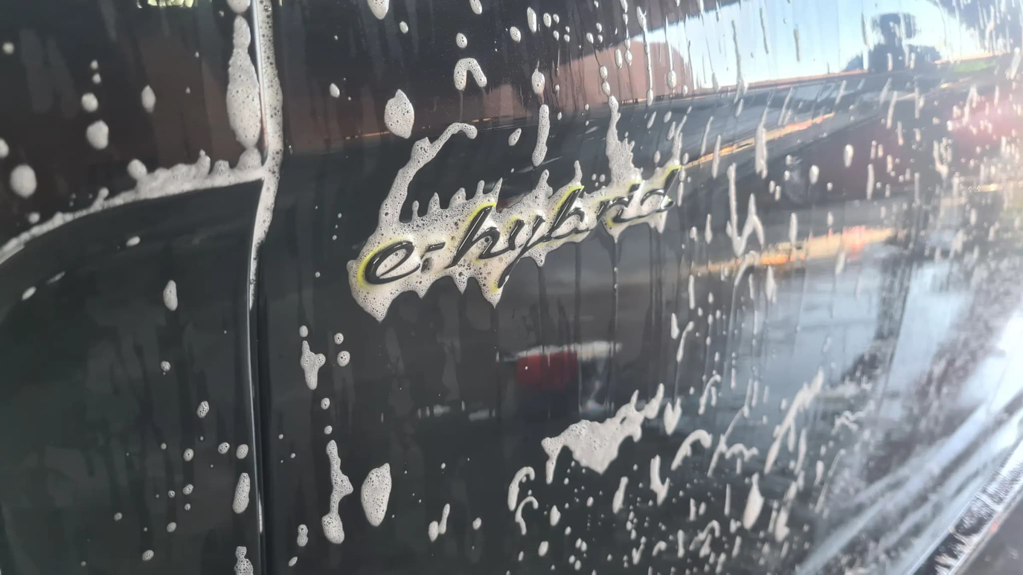Snow foam running off the coated rear quarter of a Porsche around the e-hybrid badge