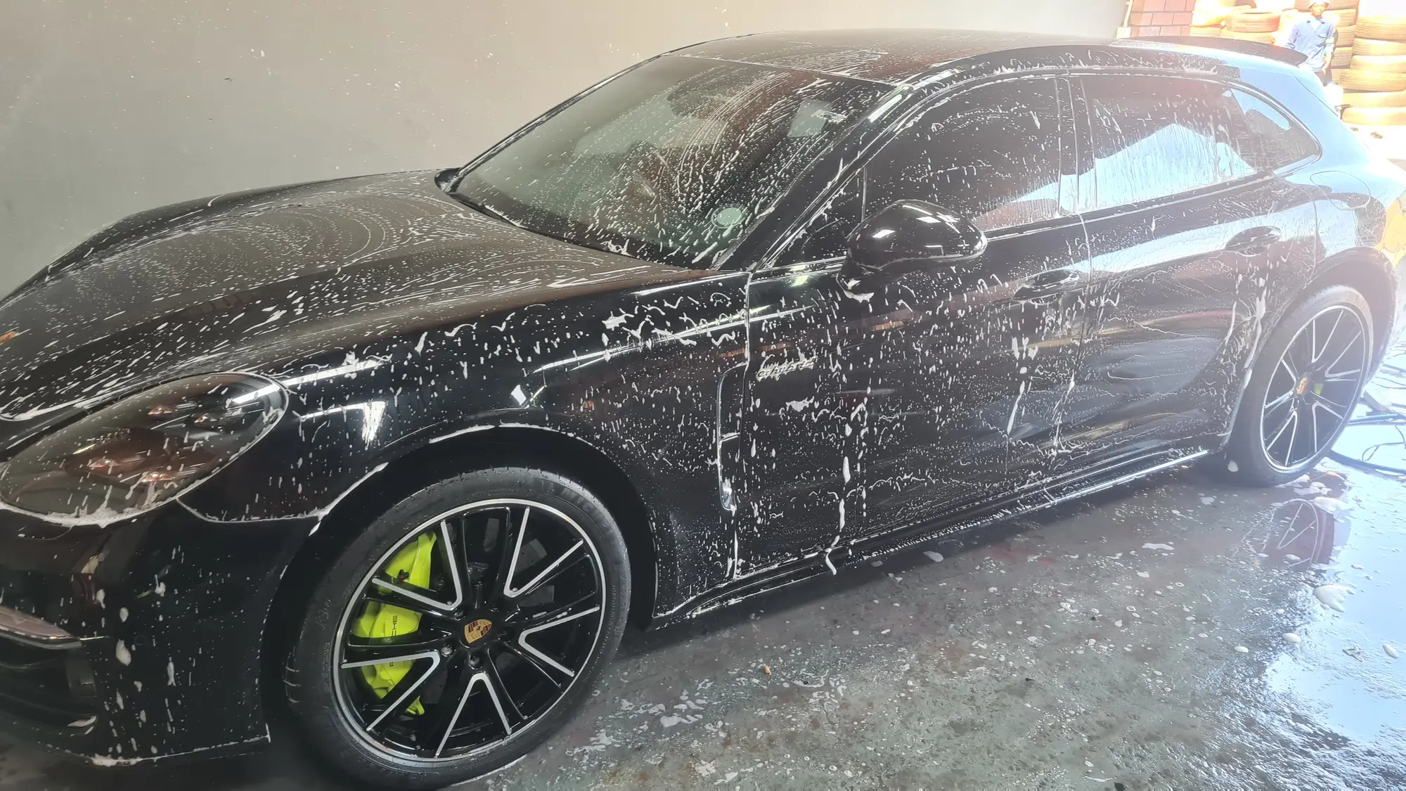A black Porsche Panamera under a full covering of snow foam before any contact wash
