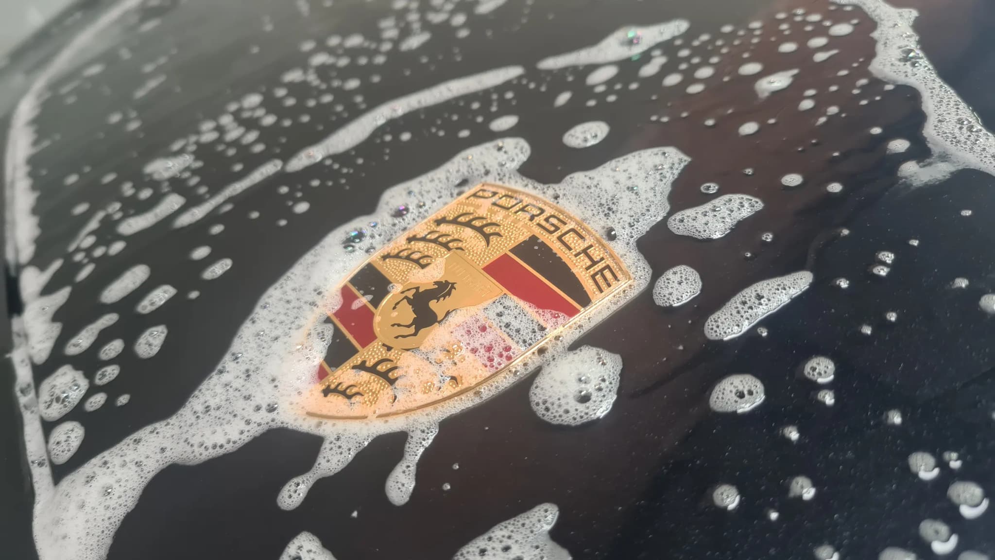 Snow foam breaking and running off the coated bonnet of a black Porsche around the crest