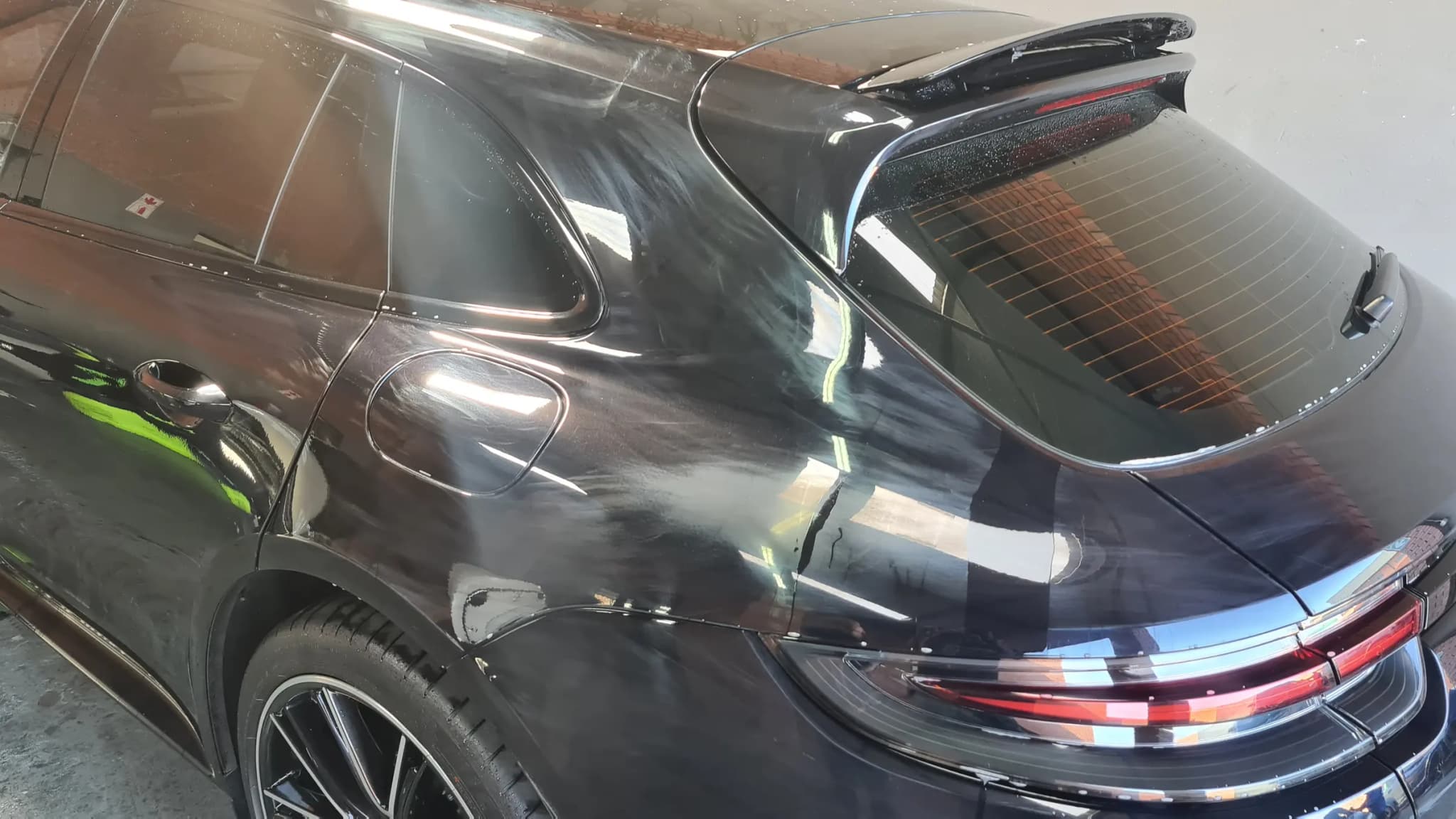 The coated flank of a black Porsche Panamera returning the yard behind it as one undistorted reflection
