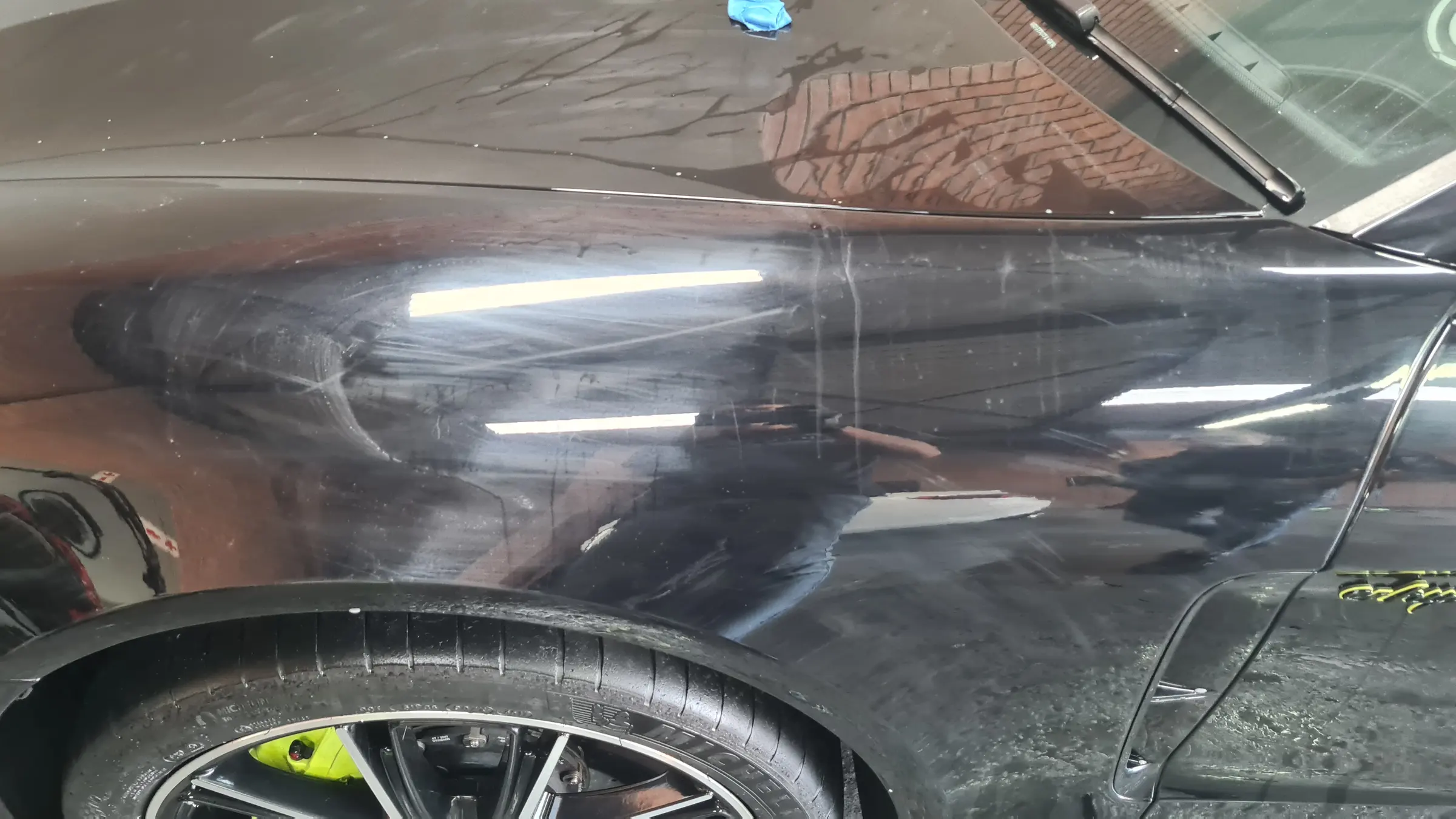 A black Porsche flank part-way through correction, compound haze still visible in the reflection