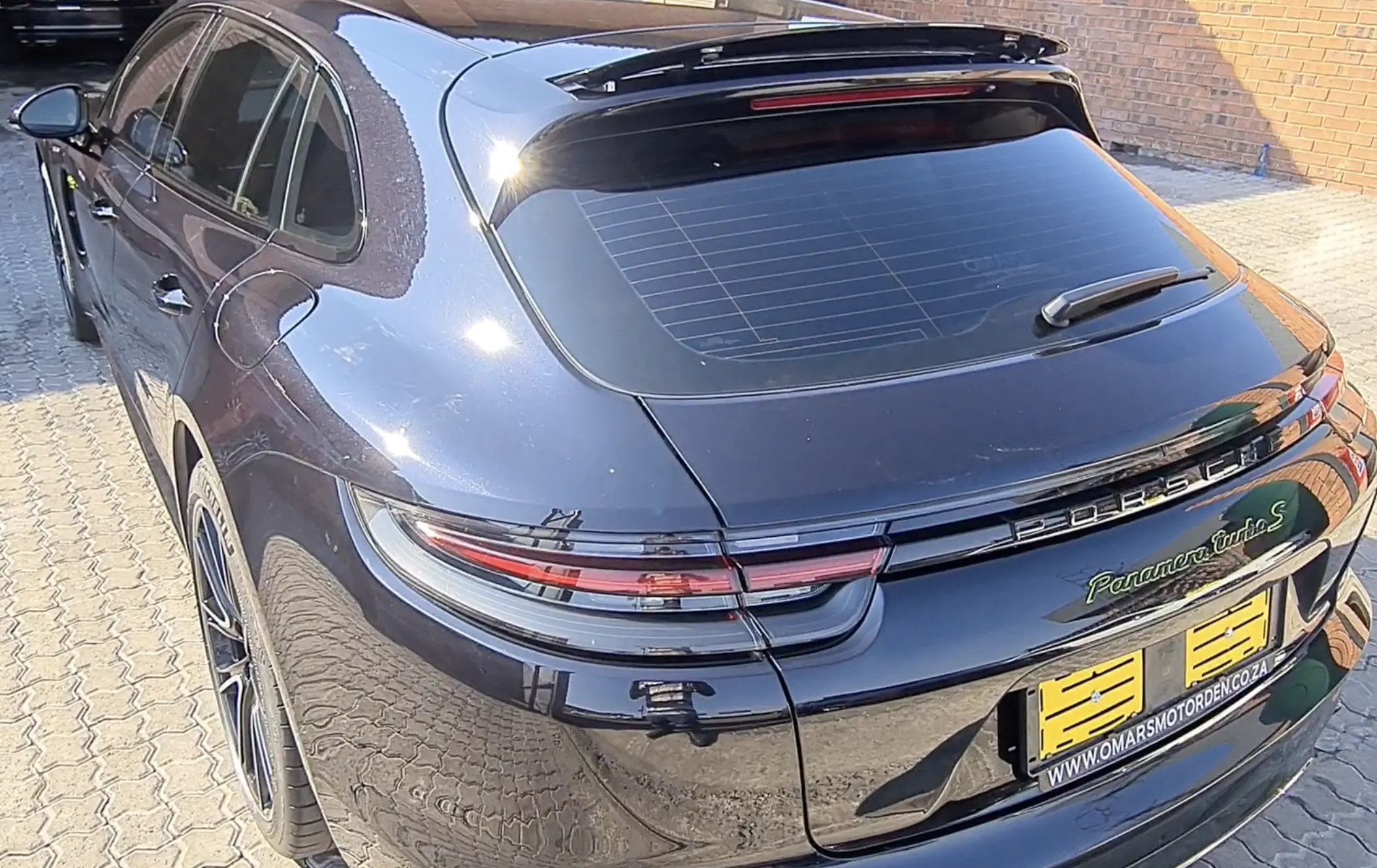 A coated black Porsche photographed from above the rear quarter, the panels returning a sharp reflection through the curve