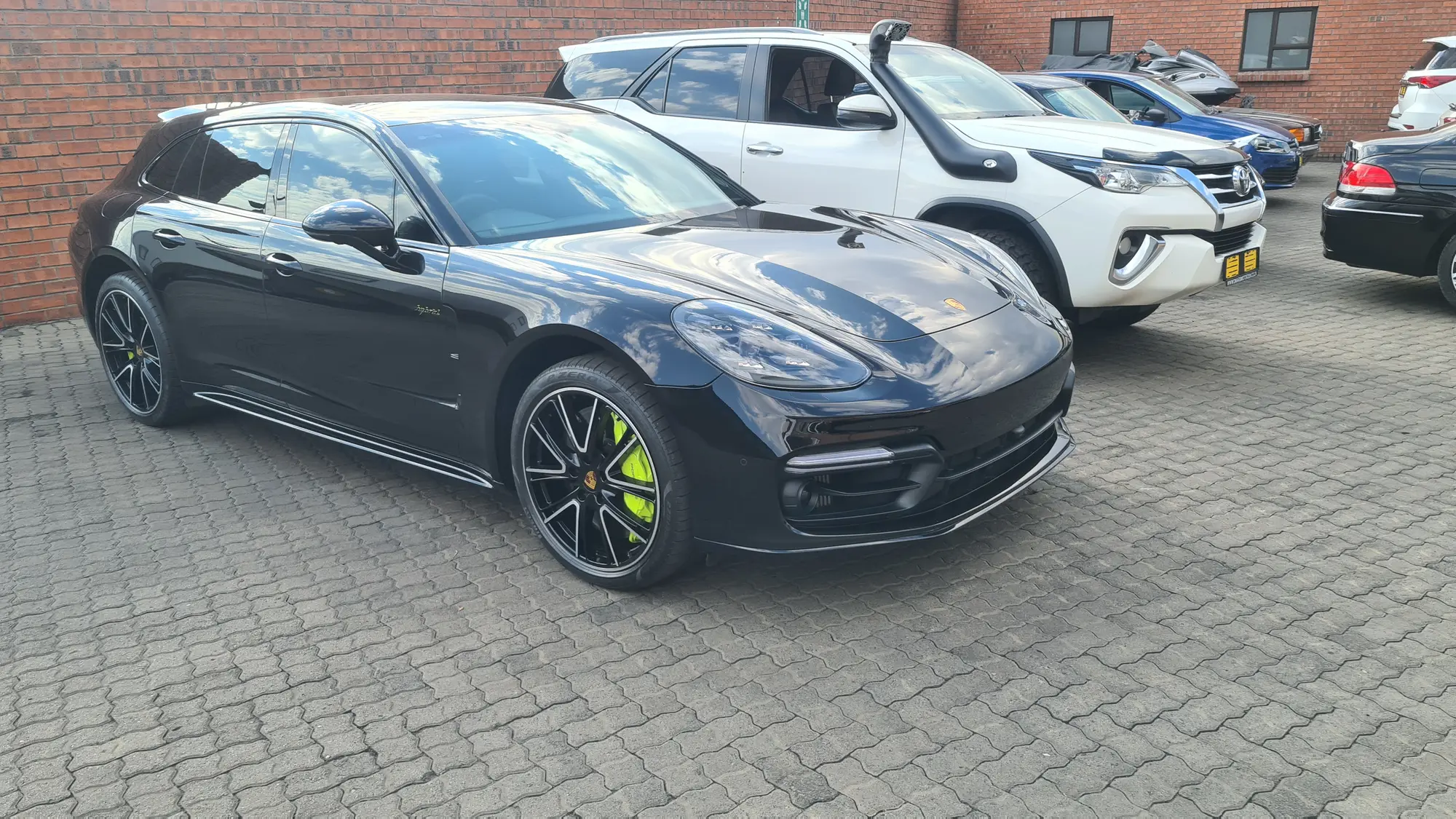 A black Porsche Panamera Sport Turismo photographed outdoors after a full detail, holding an unbroken reflection along its flank