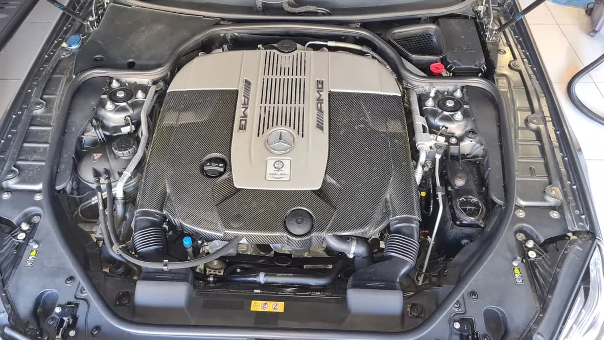 The twin-turbo V12 engine bay of a Mercedes-AMG SL 65 before cleaning, plastics dull and road film through the shuts