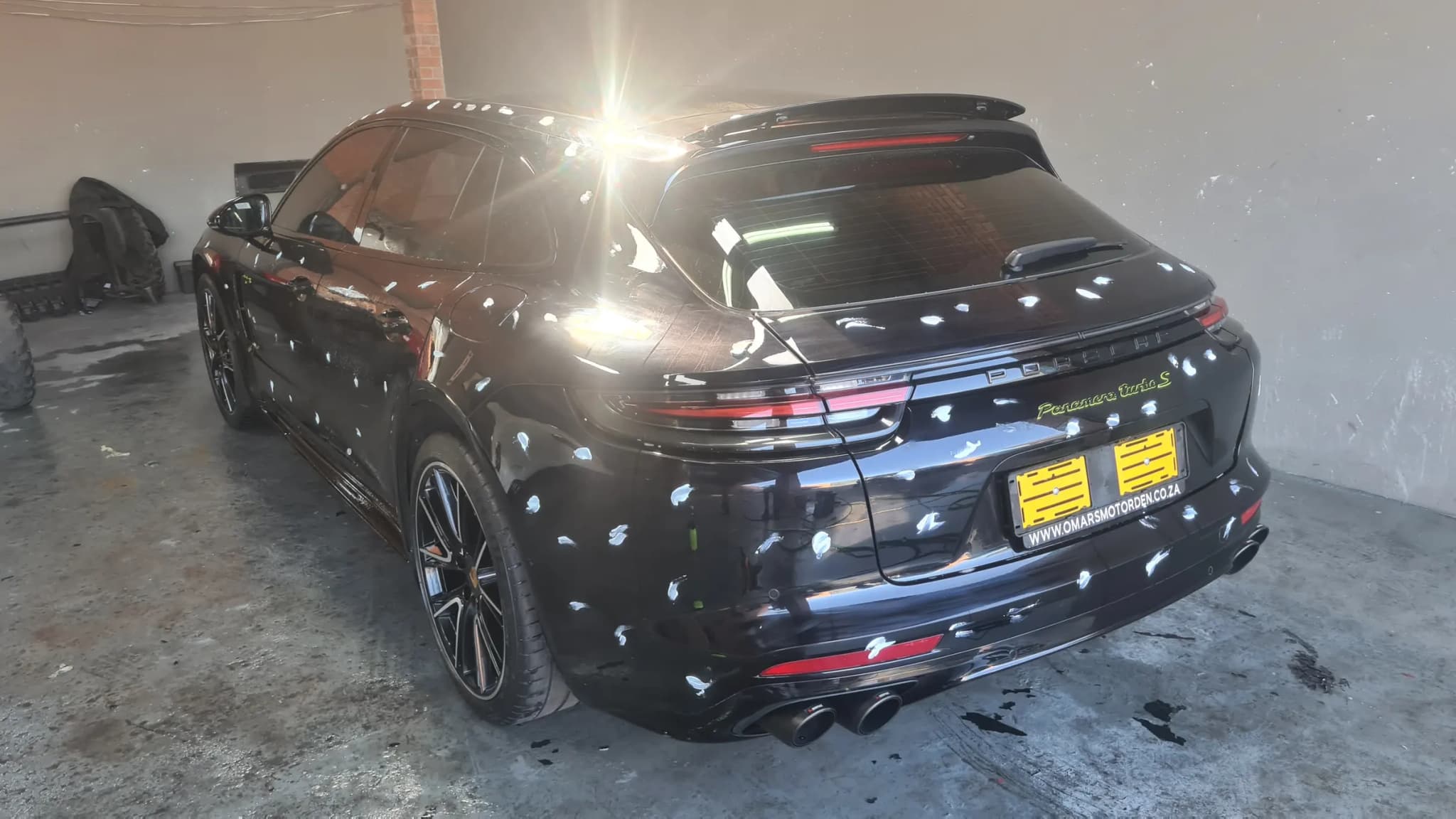 A black Porsche standing on a wet workshop floor under inspection lighting before any work begins